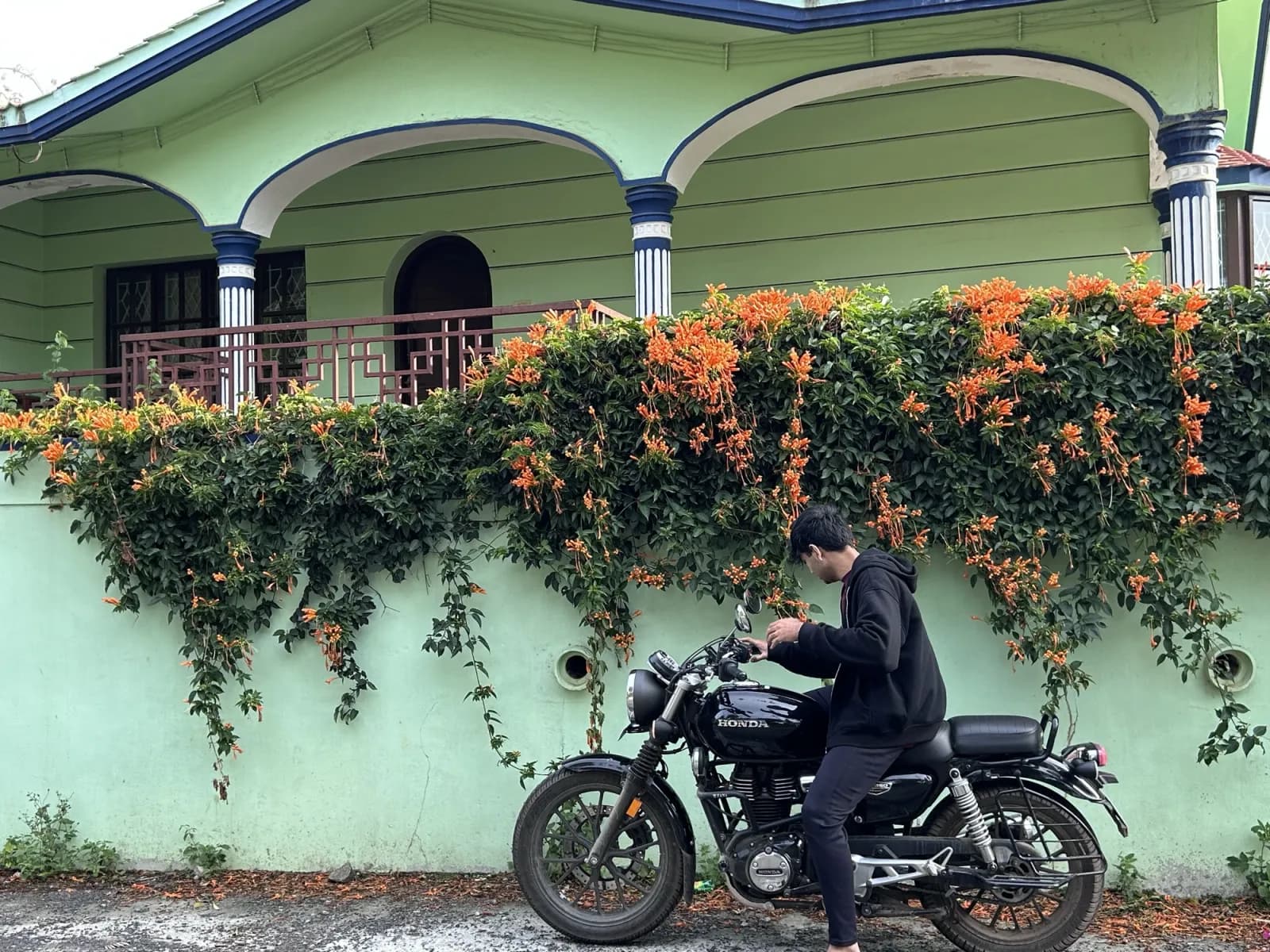A motorcycle parked beside a green house covered in orange flowers
