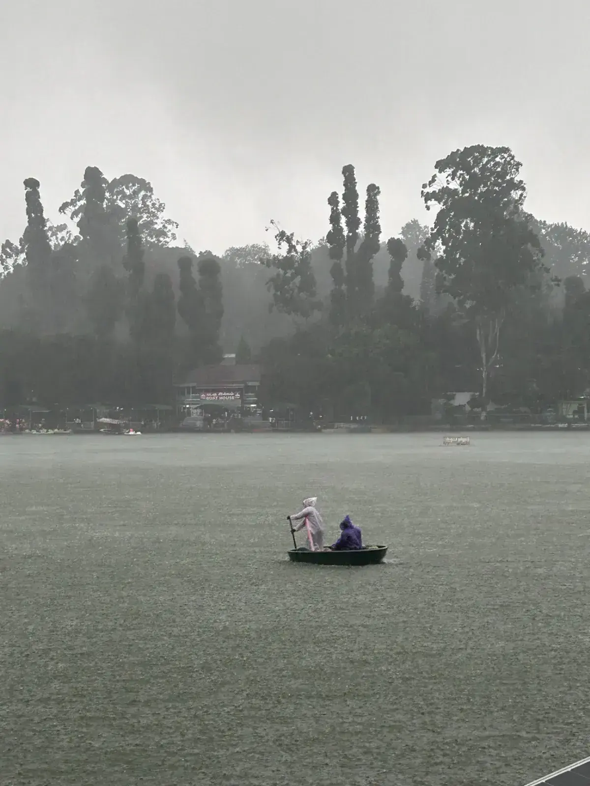 A small boat with two people on a grey lake during rain